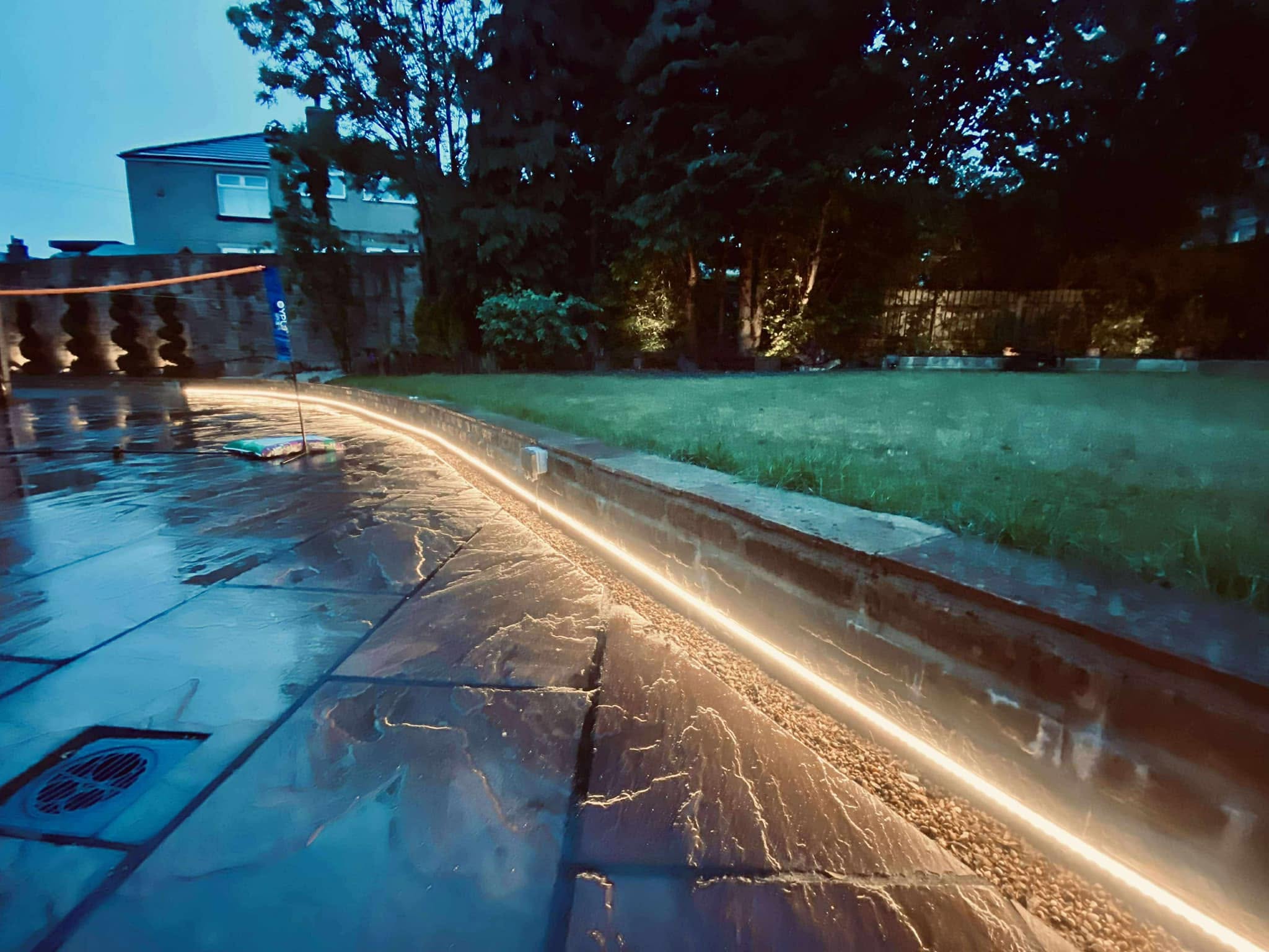 Warm linear garden lighting installed beside a patio and lawn